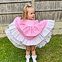 child, girl, dress, pink, white, frills, grass, outdoor, flower, hair_accessory, socks, cute, portrait, standing, fence, lawn, young_child, feet, summer, playful