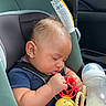 baby, car_seat, sleeping, toy, bottle, child, infant, seatbelt, inside_car, window, clothing, head, face, hand, arm, leg, plastic_toy, beads, blue_shirt, safety