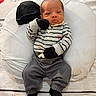 baby, infant, child, striped_clothing, mittens, hat, cushion, soft_surface, pajamas, sitting, portrait, indoor, cute, newborn, expression, face, feet, hands, cozy, resting