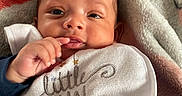 Jakel is registered to the contest to win money with this photo: baby, infant, bib, clothing, blanket, face, hand, fingers, lying_down, cute, child, portrait, expression, indoors, soft_texture, cozy, smile, young, human, sleepwear
