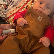 Kazdyn is registered to the contest to win money with this photo: baby, child, overalls, red_shirt, crocheted_blanket, hand, face, expression, furniture, indoor, person, toy, clown_doll, plush, couch, casual_clothing, portrait, infant, closeup, human
