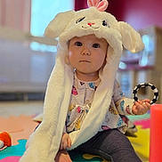 Noelle is registered to the contest to win money with this photo: baby, child, indoor, play_mat, toy, bunny_hat, cute, fluffy, costume, sitting, colorful, infant, face, expression, legging, foot, hand, clothing, room, soft_focus