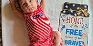 Brayleanna is registered to the contest to win money with this photo: baby, blanket, blue, cute, decor, expression, face, fireworks, indoors, infant, lying_down, person, portrait, red, sign, sock, stars, striped_clothing, text, white