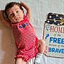 baby, blanket, blue, cute, decor, expression, face, fireworks, indoors, infant, lying_down, person, portrait, red, sign, sock, stars, striped_clothing, text, white