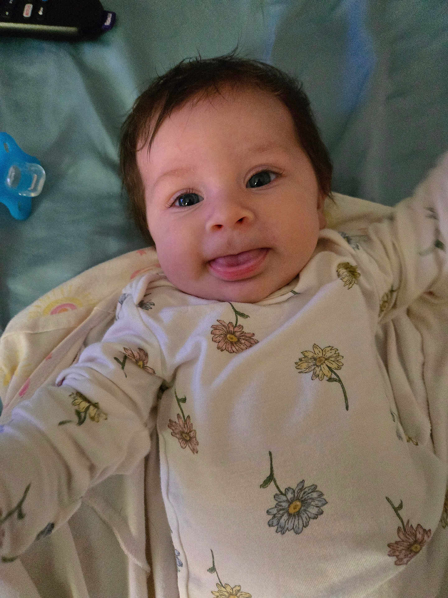 Brayleanna joined the competition — help win amazing prizes! baby, blanket, child, cute, expression, face, floral_pattern, head, indoors, infant, lying_down, onesie, pacifier, person, playful, remote_control, smiling, soft_fabric, tongue_out, young
