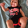 Brayleanna is registered to the contest to win money with this photo: arm, baby, bed, blanket, casual, child, clothing, cute, face, happy, indoors, infant, leg, lying_down, onesie, person, red_black, smiling, text_on_clothing, waving
