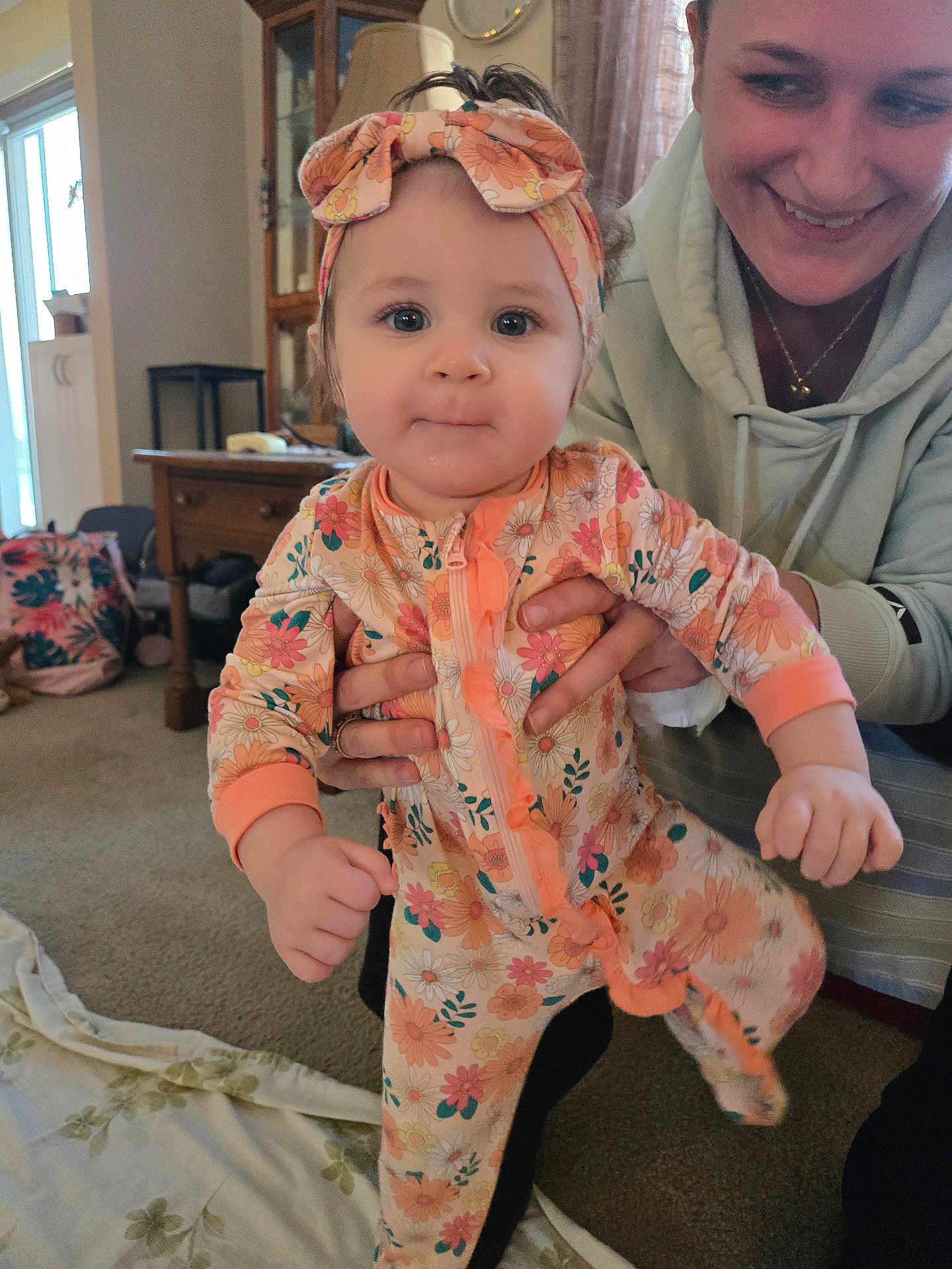 Brayleanna joined the competition — help win amazing prizes! baby, child, woman, person, indoor, living_room, carpet, onesie, headband, floral_pattern, smile, hand, furniture, curtains, cabinet, lamp, blanket, happy, portrait, family