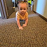 toddler, child, crawling, carpet, indoor, yellow_shirt, hair_bun, fan, clothing, room, floor, person, baby, household_items, curious, young_child, carpeted_floor, portrait, casual, home
