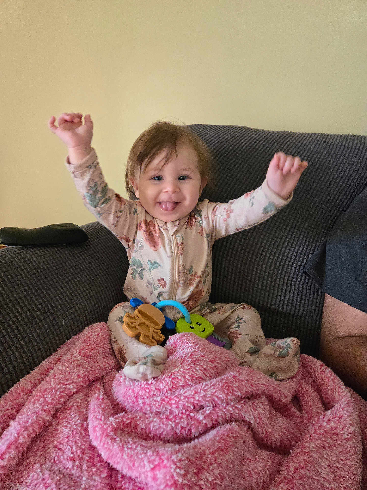 Brayleanna joined the competition — help win amazing prizes! baby, child, smiling, happy, couch, blanket, toy, pajamas, floral_pattern, arm_raised, tongue_out, indoor, person, face, hair, hand, seated, soft_texture, cozy, playful
