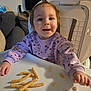 baby, cereal, cheese_puffs, child, couch, face, fox_pattern, furniture, hair, hand, happy, highchair, indoor, living_room, portrait, purple_sweater, seat, smile, snack, tray