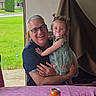 Brayleanna joined the competition — help win amazing prizes! man, child, toddler, glasses, pacifier, dress, greenery, table, can, phone, indoor, window, smile, hair, pigtails, tattoo, happy, person, family, portrait