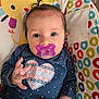 baby, pacifier, blue_shirt, heart_pattern, pony_tail, infant, baby_seat, colorful, polka_dots, smiling_sun, multicolored_circles, cute, indoors, child, portrait, hand, face, clothing, comfort, happy