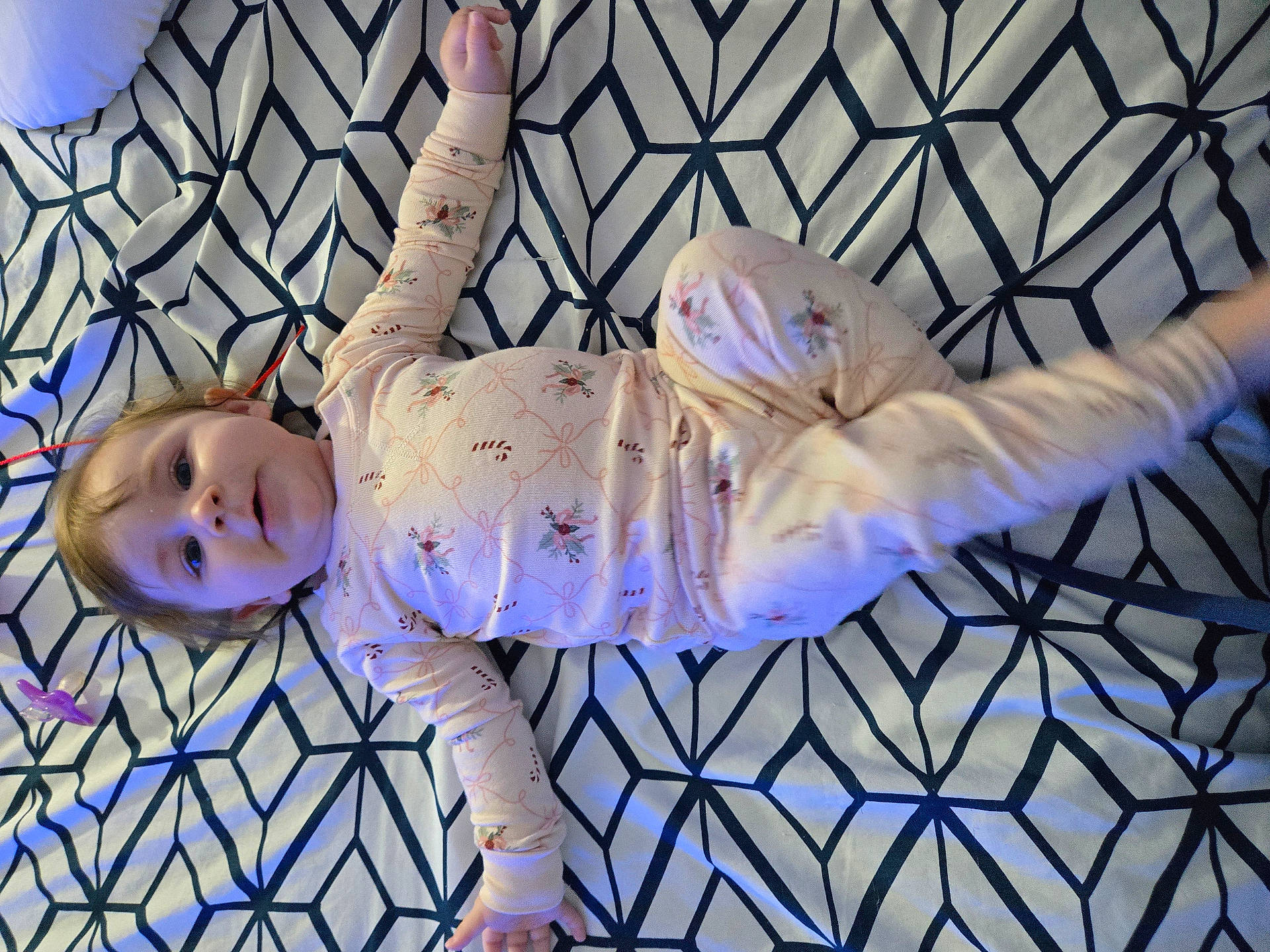 baby, bed, blanket, child, cozy, cute, face, geometric, home, indoors, infant, lying_down, pajamas, pattern, person, resting, sleepwear, smile, soft_light, young