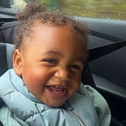 Aaliyah a rejoint le concours — aidez-le/la à gagner de superbes lots ! baby, car, car_seat, child, clothing, curly_hair, cute, face, happy, jacket, person, portrait, rain, seatbelt, side_mirror, smile, toddler, vehicle_interior, window, young_child