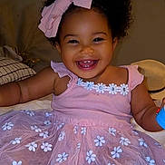 Miley joined the competition — help win amazing prizes! baby, bow, child, clothing, curly_hair, cute, cute_outfit, face, flower_pattern, happy, indoor, infant, joyful, pink_dress, playful, portrait, sitting, smiling, toddler, young_child