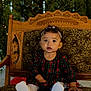 toddler, child, plaid_dress, white_shoes, headband, chair, wooden_chair, patterned_upholstery, curly_hair, indoors, holiday_lights, greenery, portrait, sitting, cute, festive, expression, young_child, baby, holiday