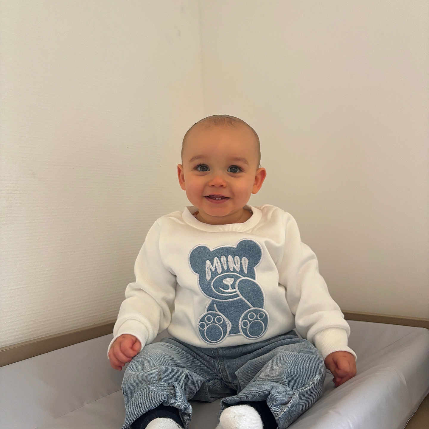 Kaïs Nomé participe au concours pour gagner de l'argent avec cette photo : baby, casual, child, clothing, cute, face, happy, head, indoor, jeans, minimalist, padded_surface, person, portrait, sitting, smiling, socks, sweatshirt, teddy_bear, wall