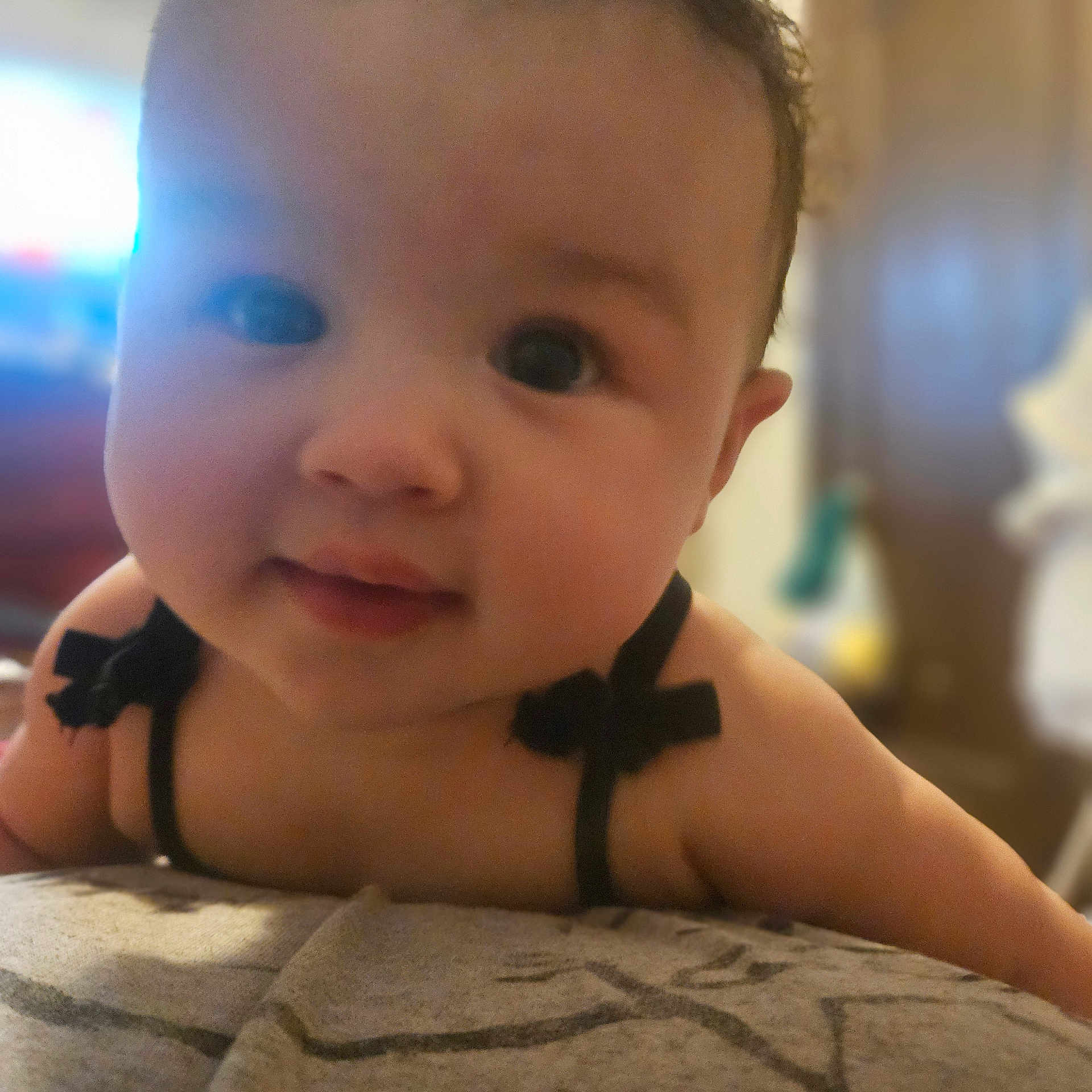 Amber is registered to the contest to win money with this photo: baby, black_clothing, bow, child, close_up, curious, cute, expression, eyes, face, focus, indoors, infant, person, portrait, shoulders, skin, smile, soft_surface, young