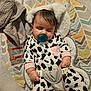 baby, blanket, child, clothing, comfort, cow_print, cushion, cute, fabric, hand, head, indoor, infant, onesie, pacifier, pattern, resting, seat, sleeping, soft