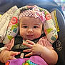 adorable, baby, car_seat, child, closeup, curious, cute, expression, face, floral_pattern, hands, headband, indoors, infant, person, pink_bow, safety_harness, sitting, toddler, young_child