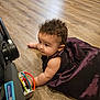 baby, child, curly_hair, purple_dress, toy, floor, wooden_floor, stroller, earrings, playing, indoor, person, infant, cute, smiling, arm, crawling, dress, colorful_toy, flooring