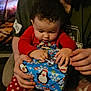 Amber is registered to the contest to win money with this photo: child, adult, gift, present, polka_dot_pants, penguin_socks, red_clothing, green_shirt, curly_hair, indoor, holiday_theme, wrapping_paper, silver_bow, hands, sitting, cozy, warm_lighting, patterned_background, family, togetherness