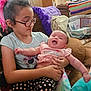 baby, blanket, child, colorful, couch, cozy, face, family, glasses, holding, home, indoor, patterned_pants, person, pillow, pink_shirt, seated, sibling, smiling, toddler