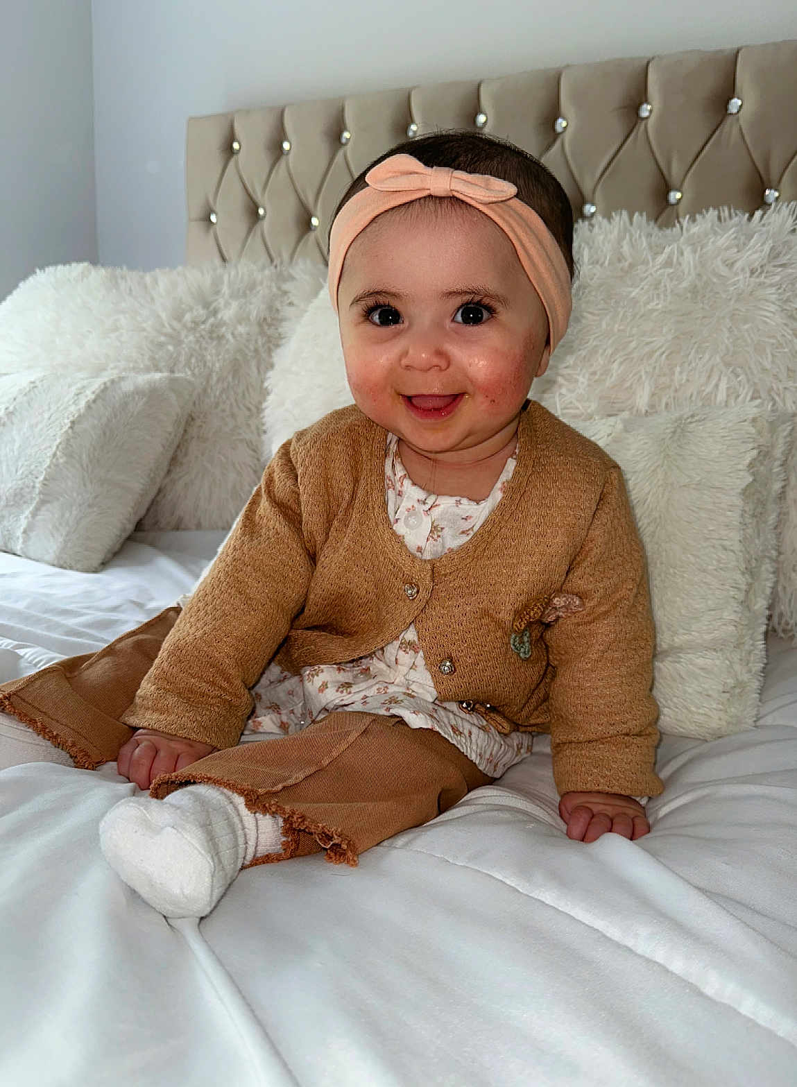 Aya a rejoint le concours — aidez-le/la à gagner de superbes lots ! baby, child, smiling, headband, brown_clothing, sitting, bed, pillow, white_bedding, soft_texture, indoor, cute, happy, portrait, infant, cozy, warm_colors, hands, feet, head