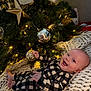Sonny is registered to the contest to win money with this photo: baby, child, christmas_tree, ornaments, lights, blanket, knit, smiling, happy, holiday, festive, indoor, decorations, gold, silver, star, person, infant, cozy, plaid