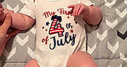 Blakley is registered to the contest to win money with this photo: 4th_of_july, baby, blanket, celebration, chubby_legs, clothing, cute, hand, happy, holding_hand, human, indoors, infant, laying_down, onesie, pattern, person, skin, smiling, young_child