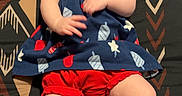 Blakley is registered to the contest to win money with this photo: baby, infant, smiling, dress, headband, patterned_blanket, cute, lying_down, happy, chubby_legs, tongue_out, red_shorts, blue_dress, skin, child, indoors, person, young, playful, comfortable
