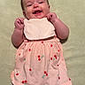 Blakley is registered to the contest to win money with this photo: baby, infant, smiling, dress, pink, cherry_print, black_shorts, blanket, hand, happy, cute, lying_down, child, person, apparel, toddler, skin, face, young, indoors