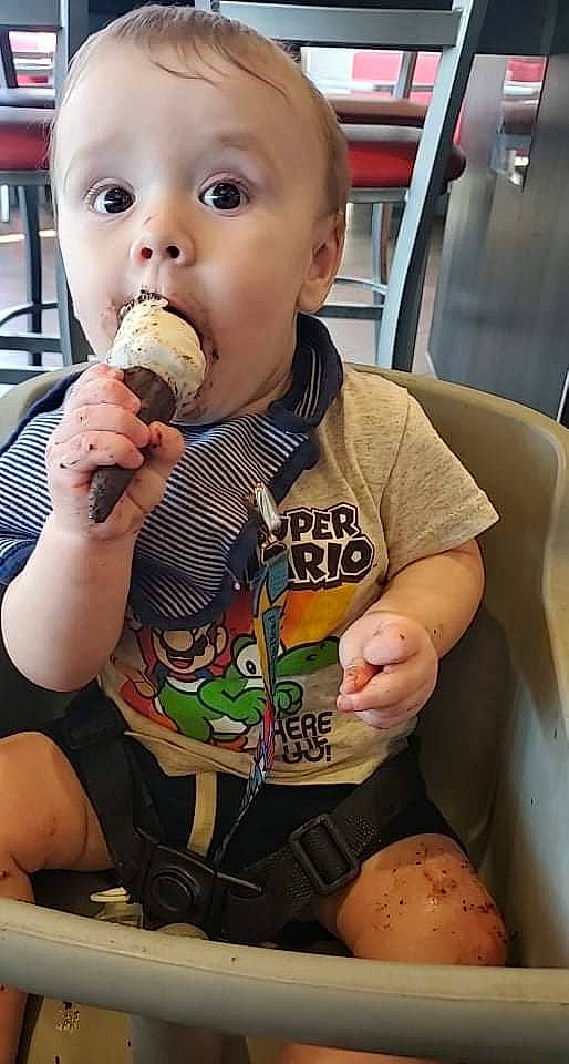 Raylan is registered to the contest to win money with this photo: arm, baby, baby_toddler_clothing, biting, chair, child, dairy, drinkware, facial_expression, finger, food, food_craving, hand, mouth, nail, nose, person, sleeve, surprise, thigh