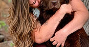 Hazel is registered to the contest to win money with this photo: person, dog, hug, outdoor, tree, nature, brown_dog, affection, love, pet, animal, long_hair, casual_clothing, sandals, close_up, portrait, happy, companionship, friendship, warmth