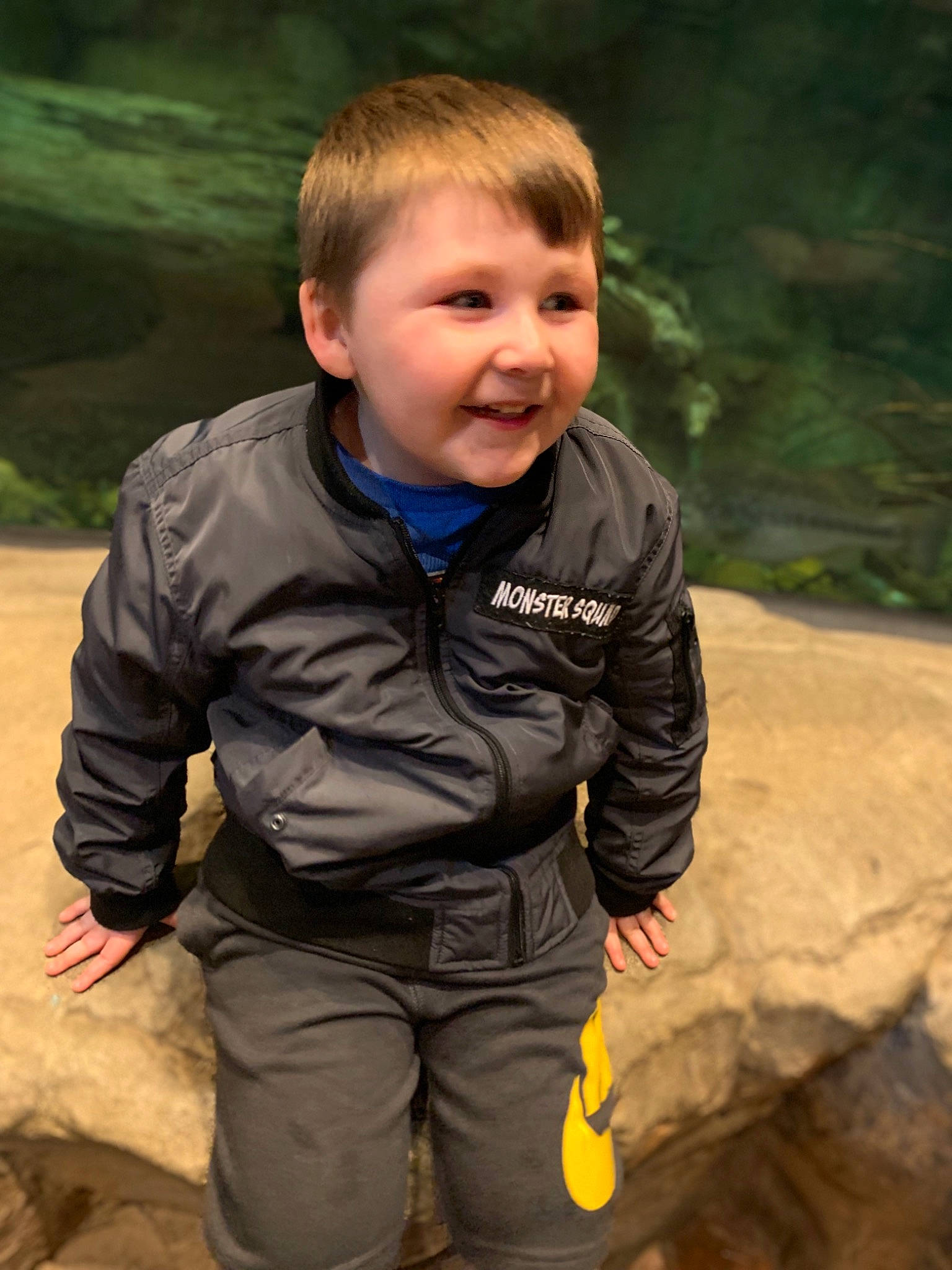 Bentley is registered to the contest to win money with this photo: cheek, child, eye, face, fun, grass, jacket, male, outerwear, people, person, photography, play, recreation, sitting, skin, smile, standing, toddler, tree