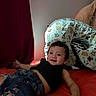 toddler, child, smile, happy, bed, pillow, teddy_bear, denim_shorts, black_top, floral_pattern, animal_print, indoor, red_bedspread, curtain, cozy, cute, portrait, relaxed, furniture, person