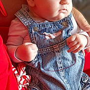 Tylio participe au concours pour gagner de l'argent avec cette photo : baby, infant, denim_overalls, clothing, person, child, hand, face, skin, red_clothing, seated, closeup, portrait, casual, indoor, cute, young, newborn, curious, soft_lighting