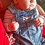 baby, infant, denim_overalls, clothing, person, child, hand, face, skin, red_clothing, seated, closeup, portrait, casual, indoor, cute, young, newborn, curious, soft_lighting