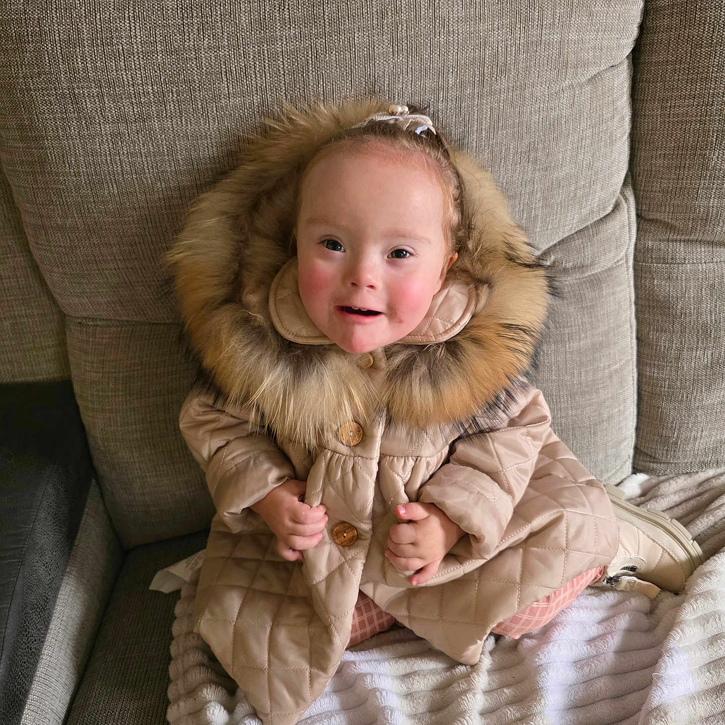 Jasmine is registered to the contest to win money with this photo: baby, blanket, child, clothing, coat, cozy, cute, fur_hood, furniture, happy, headwear, indoor, person, portrait, quilted_coat, sitting, smile, sofa, toddler, warm