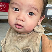 Mung is registered to the contest to win money with this photo: baby, child, face, eyes, hand, bib, clothing, indoor, person, portrait, cute, infant, skin, expression, holding, young, human, apparel, closeup, soft_lighting
