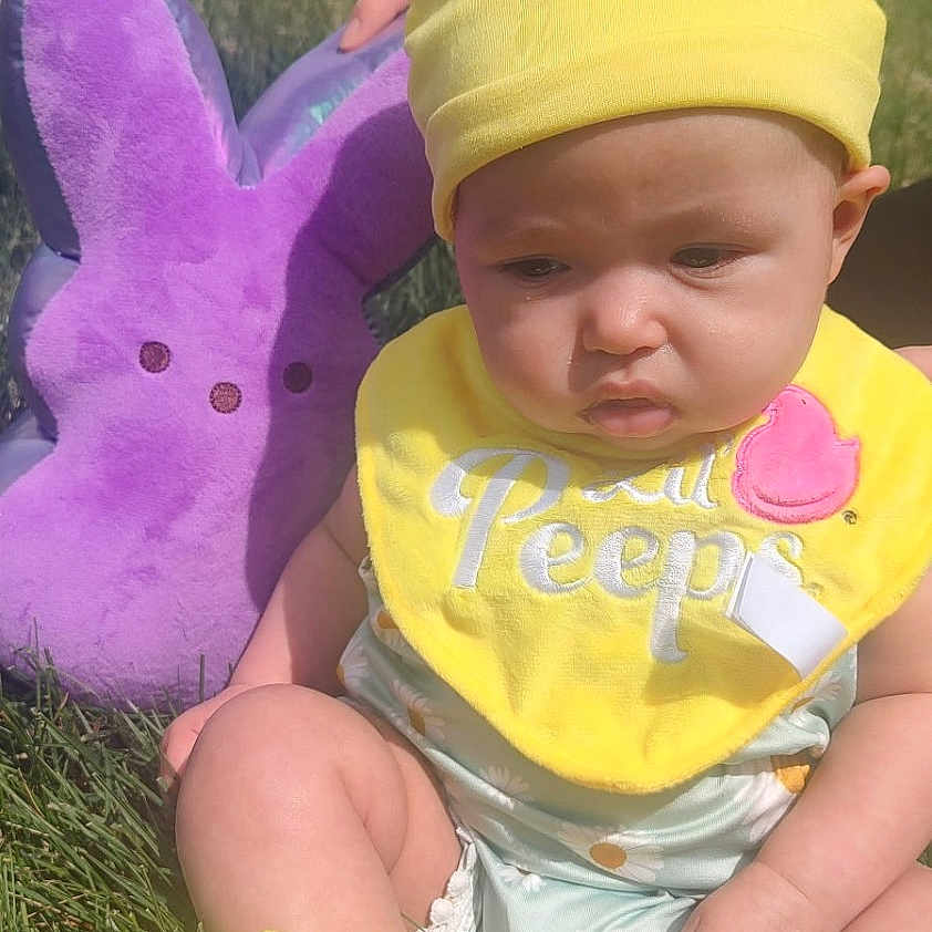 Lailah is registered to the contest to win money with this photo: baby, cap, clothing, costume, face, glove, grass, hat, head, nature, outdoors, park, person, photography, plant, portrait, purple, soil, t_shirt, toy