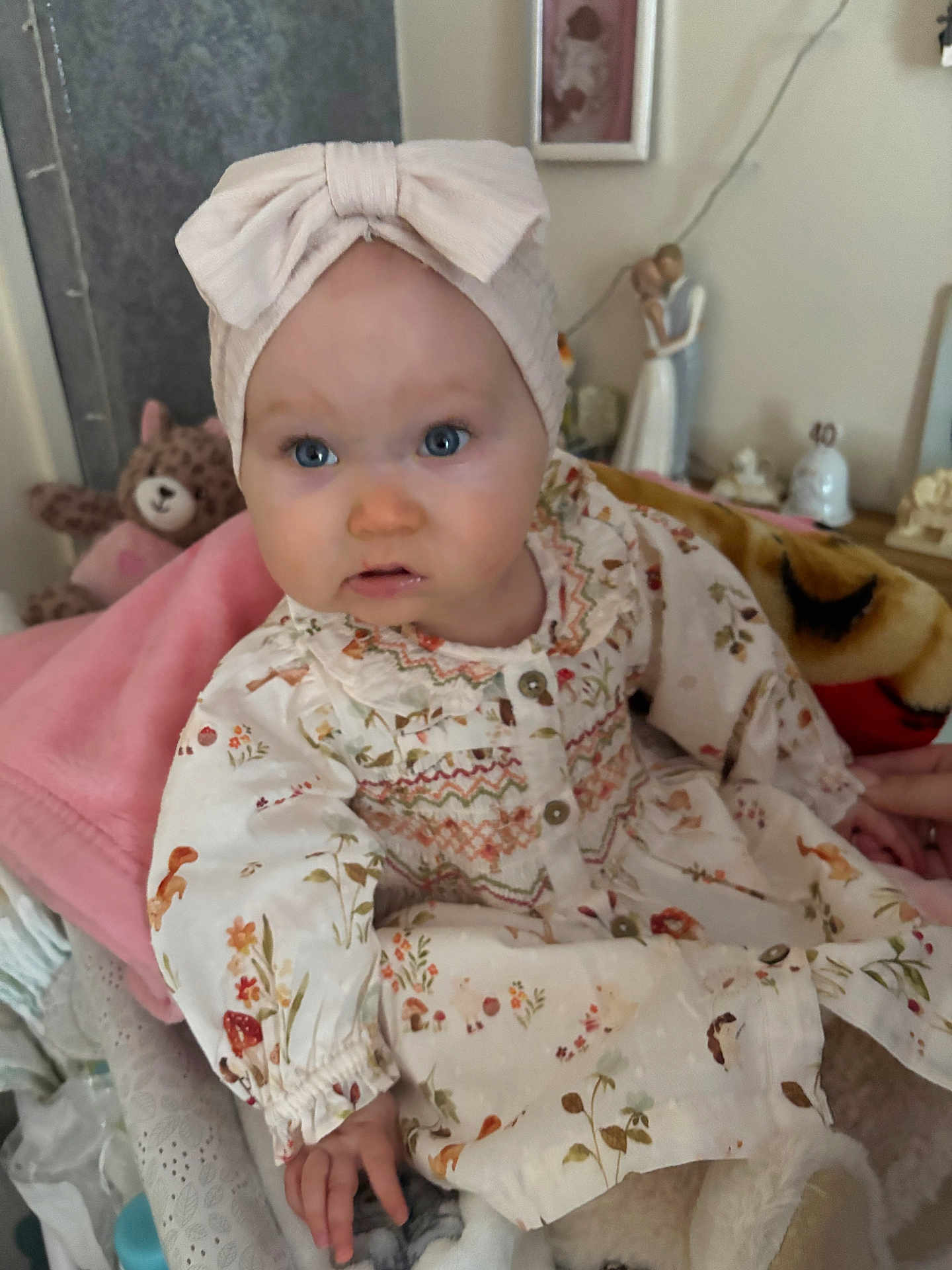 Skylar is registered to the contest to win money with this photo: baby, child, blue_eyes, headband, bow, floral_dress, blanket, stuffed_toy, teddy_bear, indoor, portrait, cute, infant, soft_toys, furniture, hand, face, clothing, smile, person
