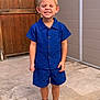 blue_clothing, boy, casual, child, cute, eyes_closed, happy, outdoor, person, portrait, shirt, shorts, smiling, sneakers, standing, stone_patio, summer, wall, wooden_door, young