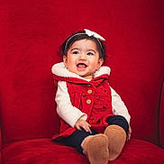 Aria joined the competition — help win amazing prizes! baby, child, smiling, red_chair, red_vest, white_bow, headband, happy, portrait, sitting, indoors, cozy, clothing, cute, face, person, young_child, apparel, footwear, warm