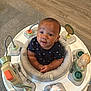 Jasai is registered to the contest to win money with this photo: baby, infant, activity_center, toys, floor, carpet, wood_floor, child, smiling, sitting, cushion, play, indoor, cute, curious, clothing, face, hands, head, expression
