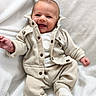 baby, smiling, infant, clothing, jacket, pants, white_blanket, cozy, cute, happy, face, portrait, child, soft_texture, sitting, small_hands, newborn, indoors, warm, casual_wear