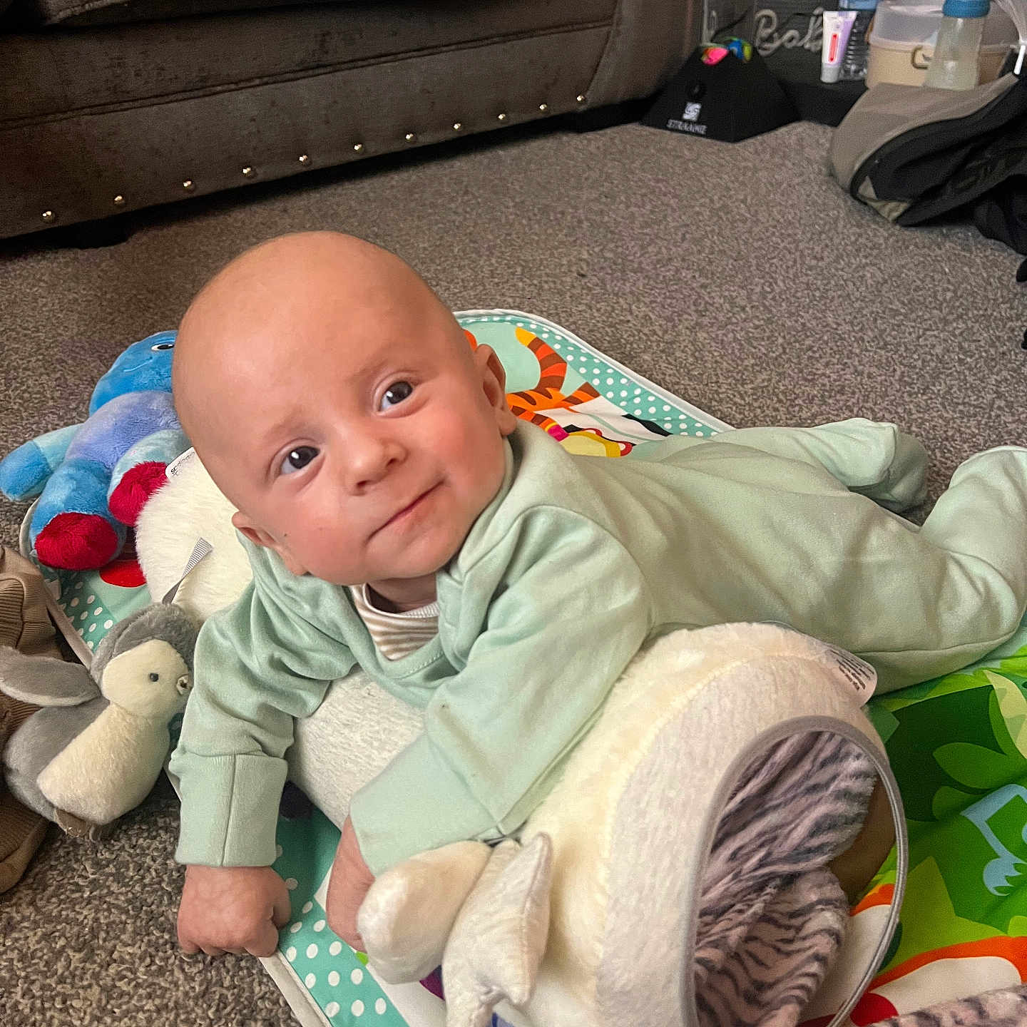 Romie is registered to the contest to win money with this photo: baby, carpet, child, clothing, comfort, cute, face, floor, head, home, indoors, infant, living_room, lying_down, person, play_mat, plush_toys, smiling, sofa, soft_toys
