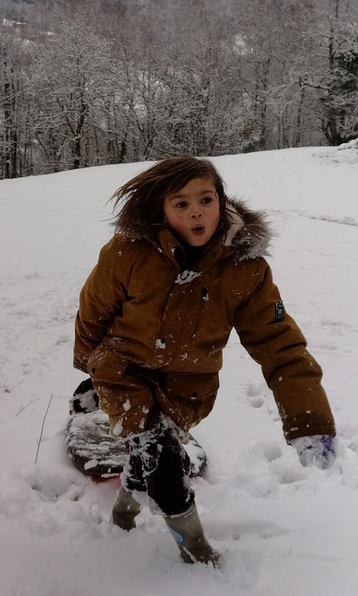 Ellia participe au concours pour gagner de l'argent avec cette photo : beauty, brown_hair, cheek, freezing, fun, fur, glove, happy, hoodie, jacket, mammal, parka, person, sitting, sleeve, snow, snow_boot, surprise, toddler, tree