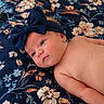 baby, infant, headband, bow, blue, blanket, floral_pattern, plush_toy, teddy_bear, bed, resting, skin, face, eyes, cute, child, soft_toy, indoors, comfort, portrait