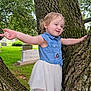 toddler, child, tree, outdoor, nature, greenery, dress, denim, arms_outstretched, smiling, grass, trunk, person, young_child, playful, park, daylight, happy, casual_clothing, forest